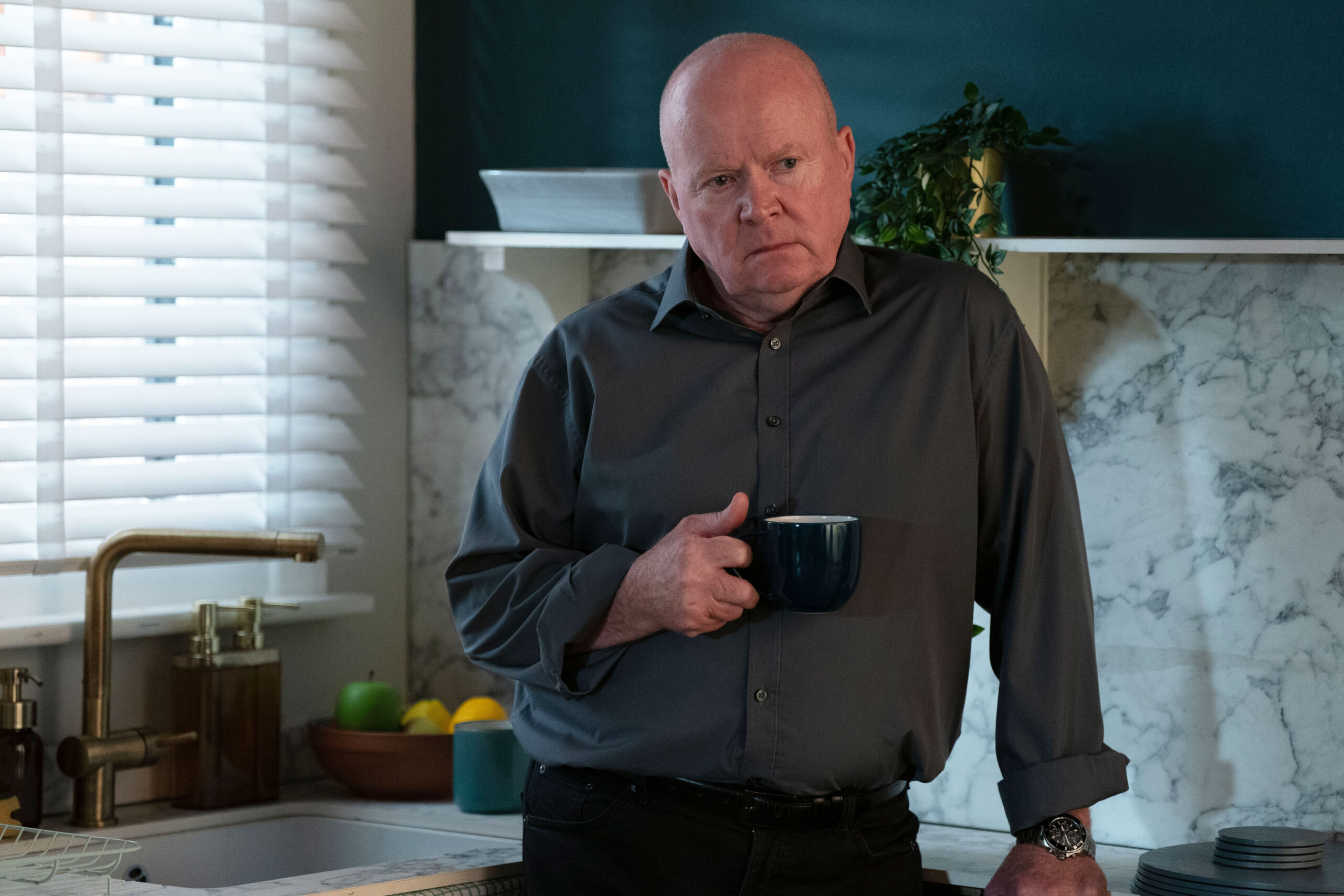 Phil Mitchell is holding a cup of tea and looking sad