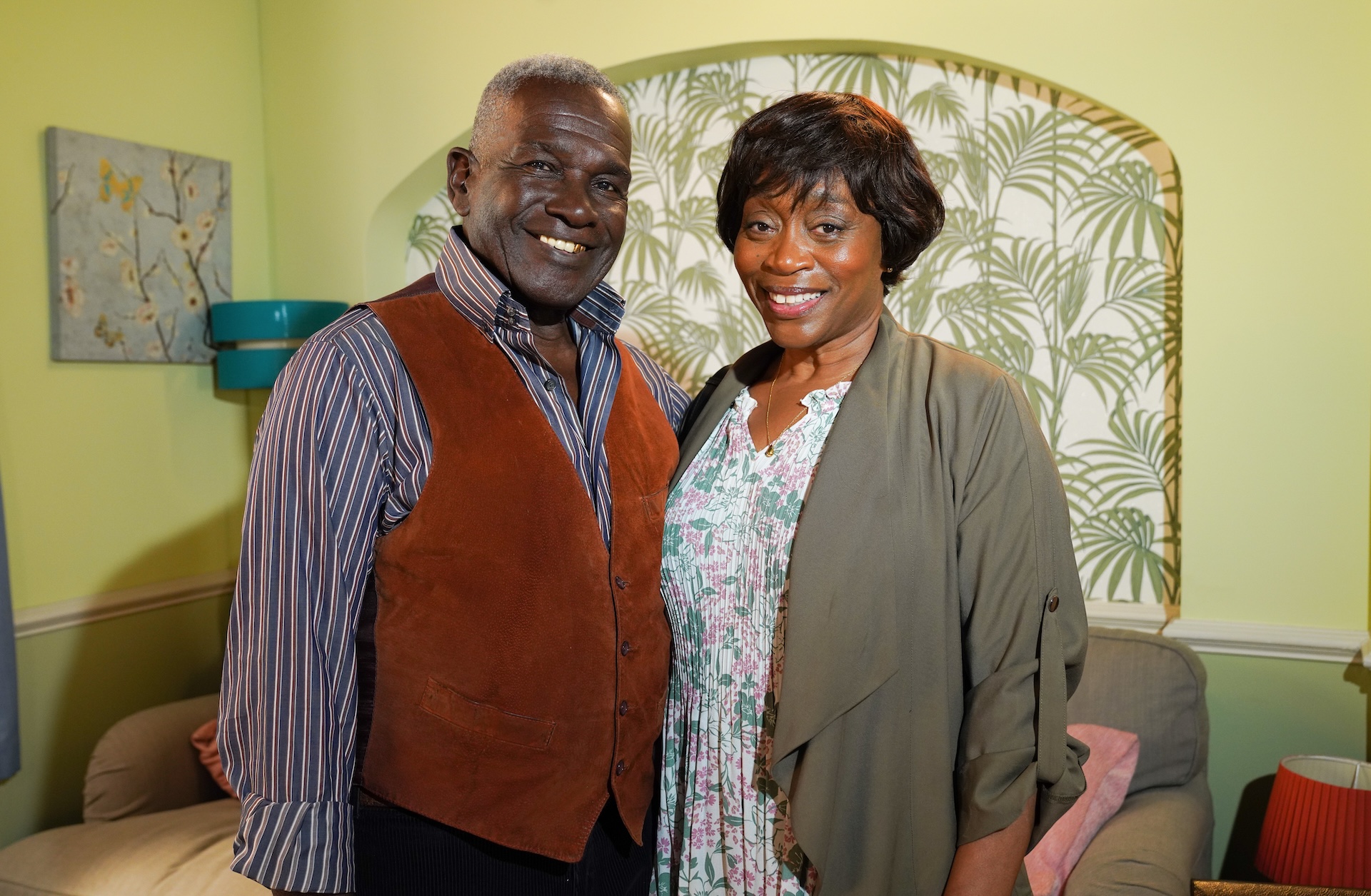 Patrick and Yolande smiling as they stand next to each other at home on EastEnders