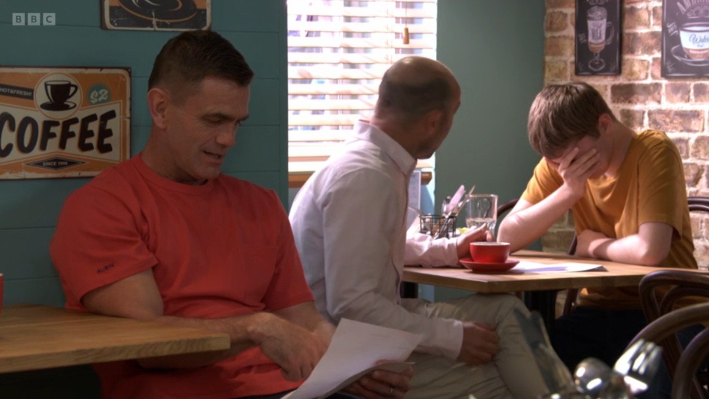 Barney with his head in his hands in the cafe on EastEnders (Credit: BBC/Composite: EI)
