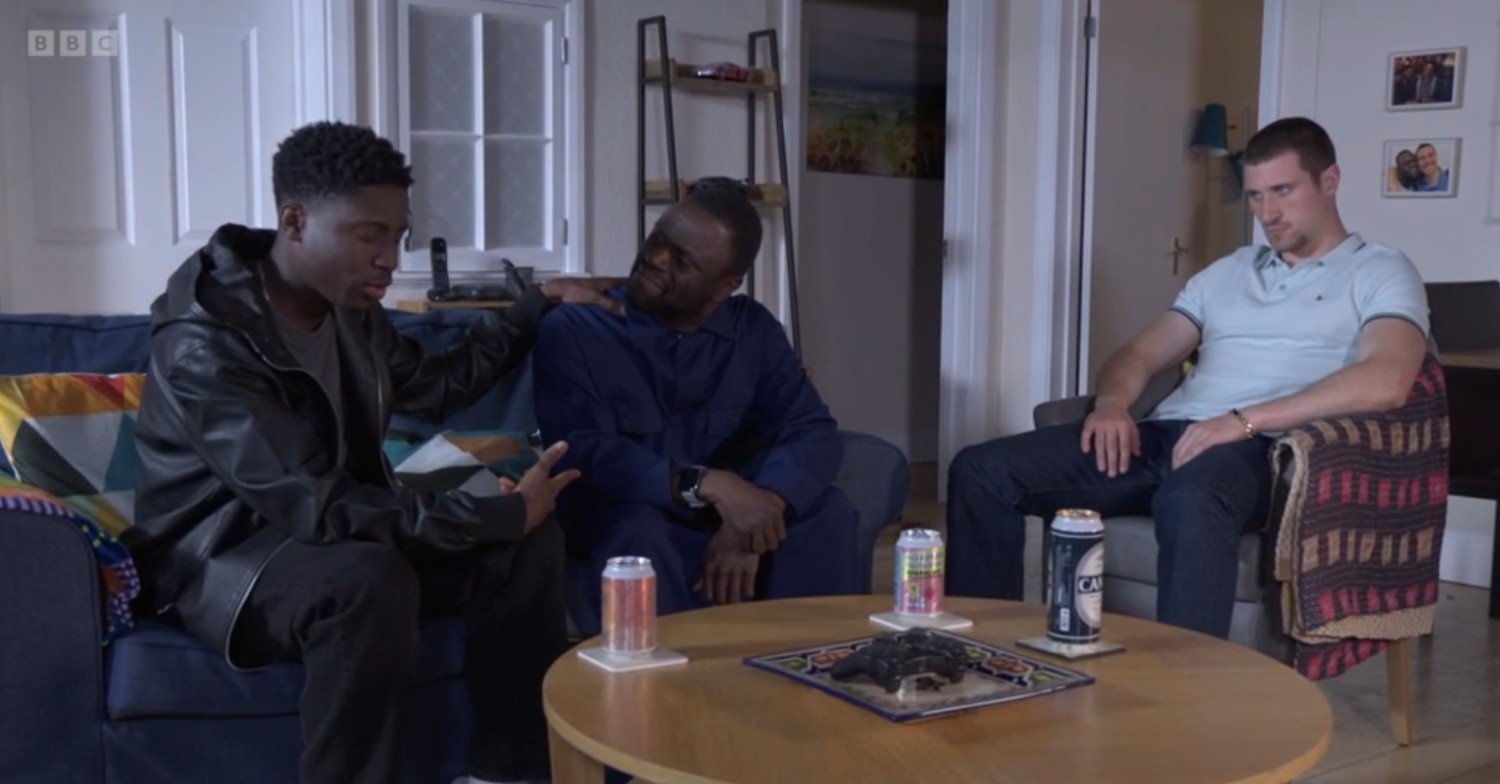 Okie and Kojo talk on the sofa while Harry sits in the background sulking