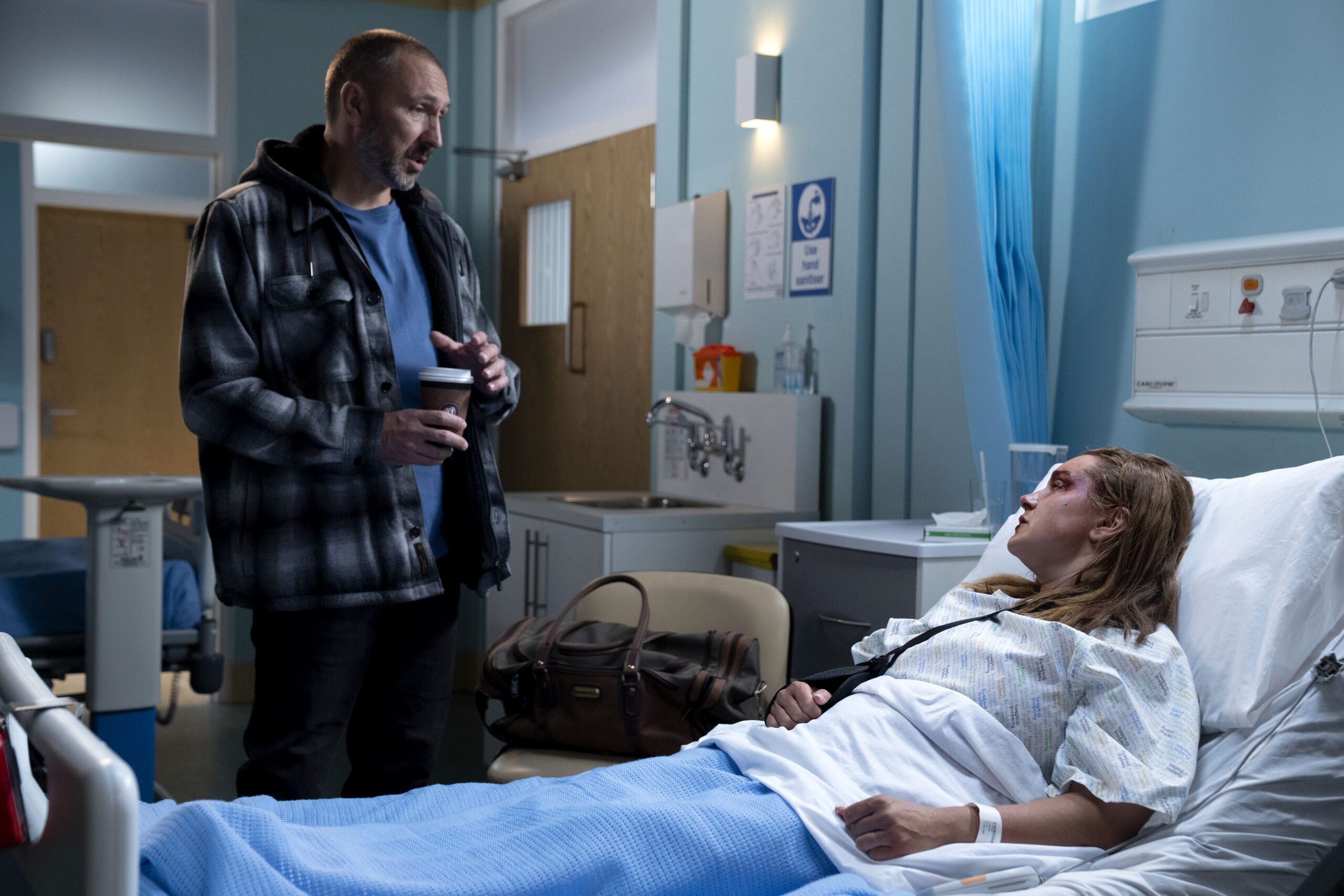 Ross stands over Vicki, who's in a hospital bed