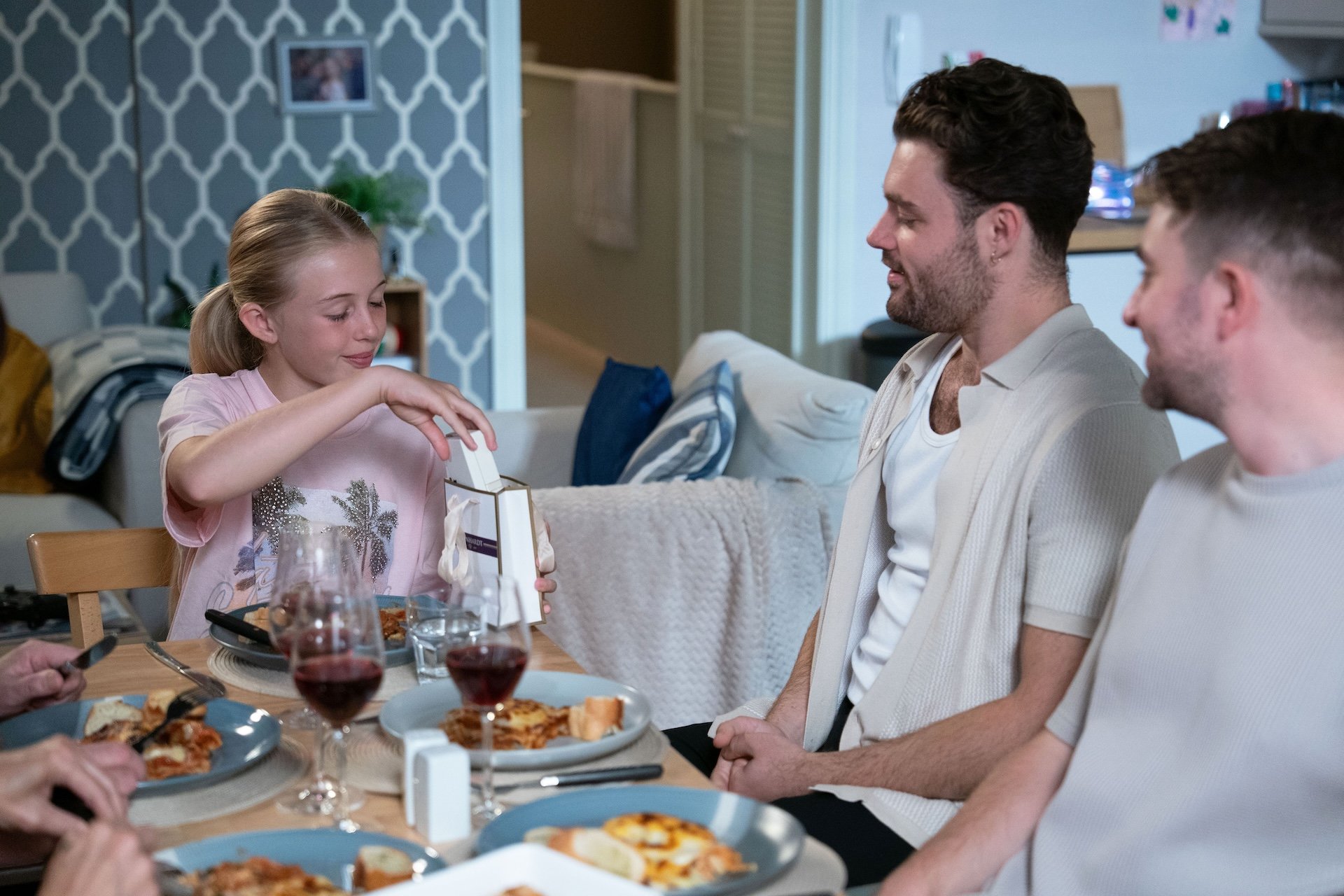 Lexi's happy as she opens a gift from Johnny while Callum looks on