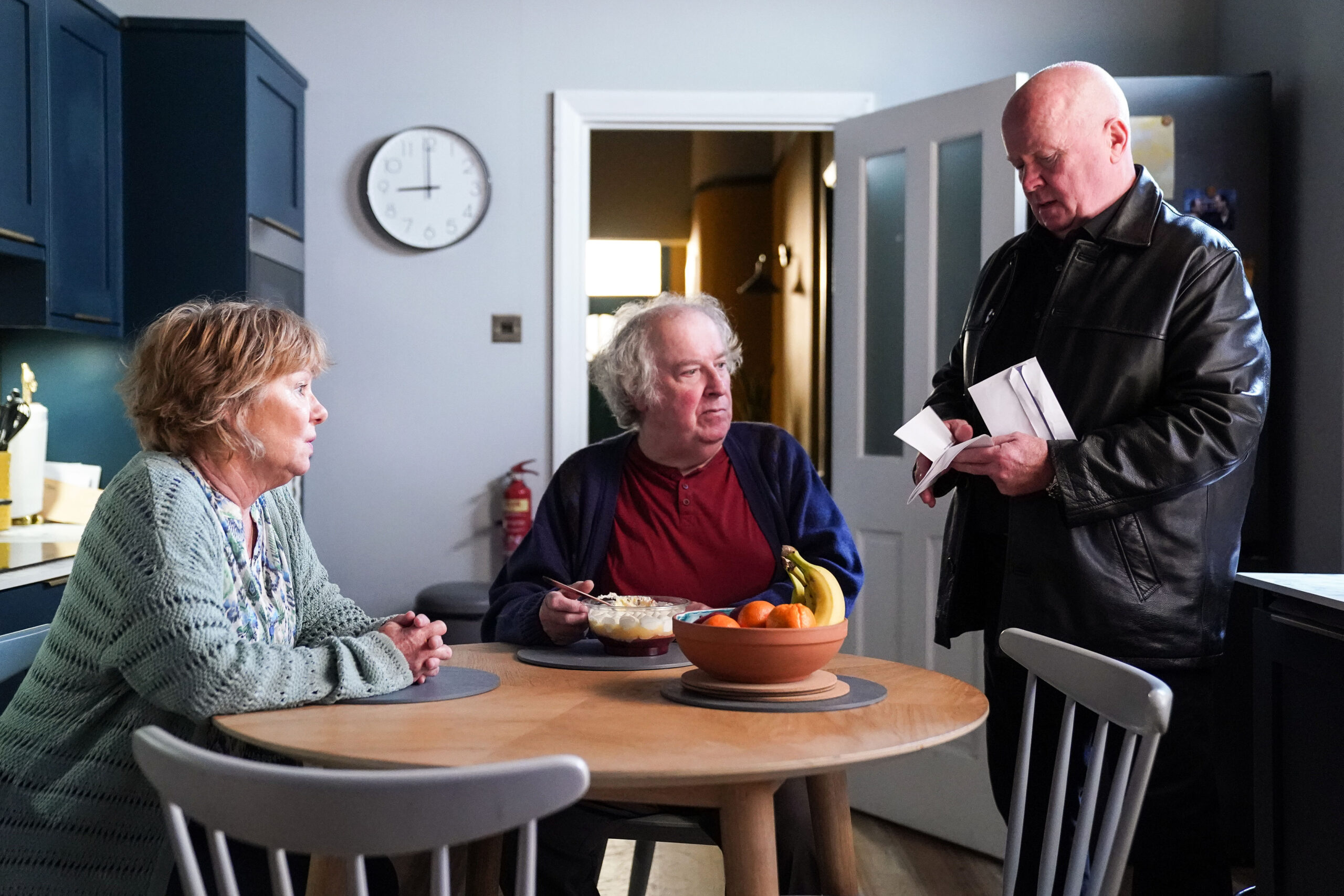 Phil looks at a piece of paper as Julie and Nigel sit around the kitchen table