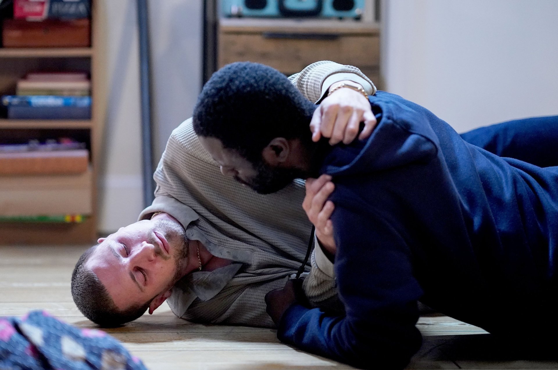 Kojo holds Harry, who lies on the floor in a state