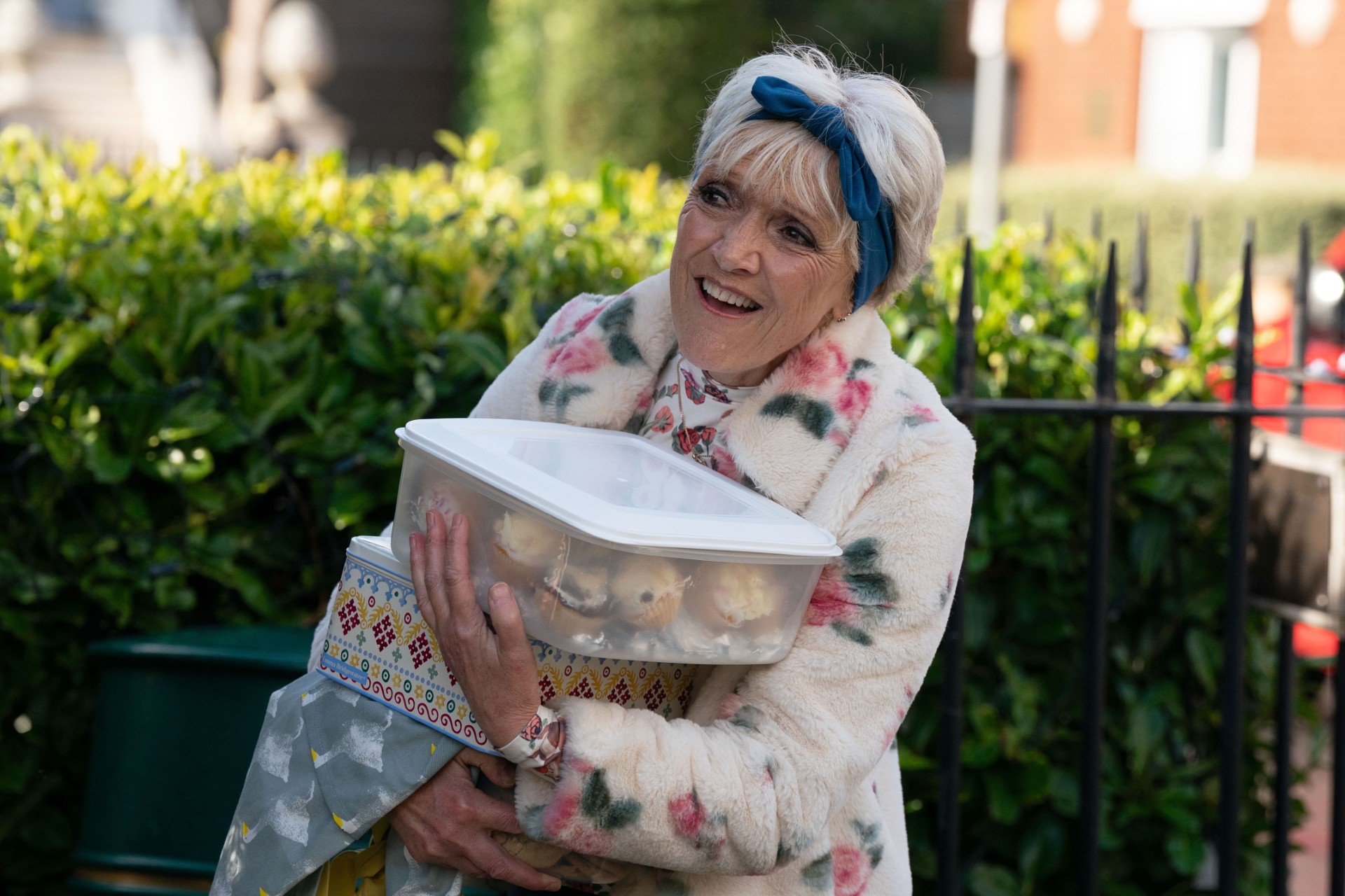 Jean carrying a gift and a box of cupcakes