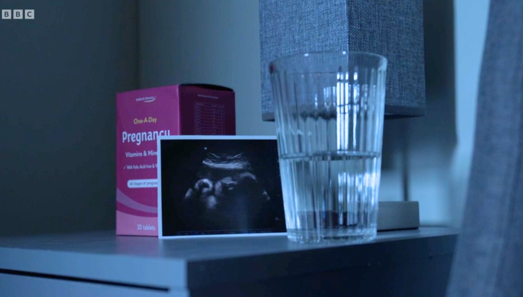 A pregnancy test box and baby scan on a bedside table