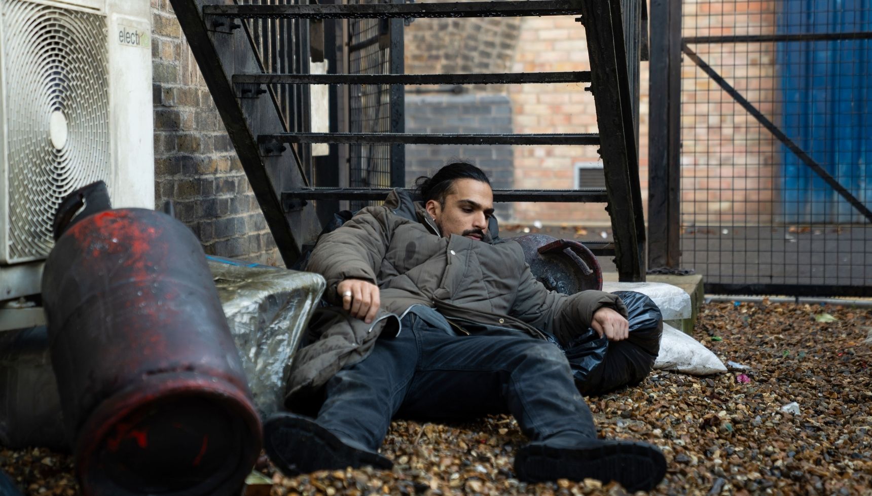 Ravi wakes up next to some bins after being spiked 