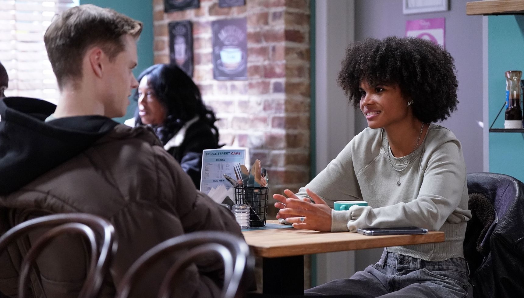 Jasmine and Oscar chat in the cafe 