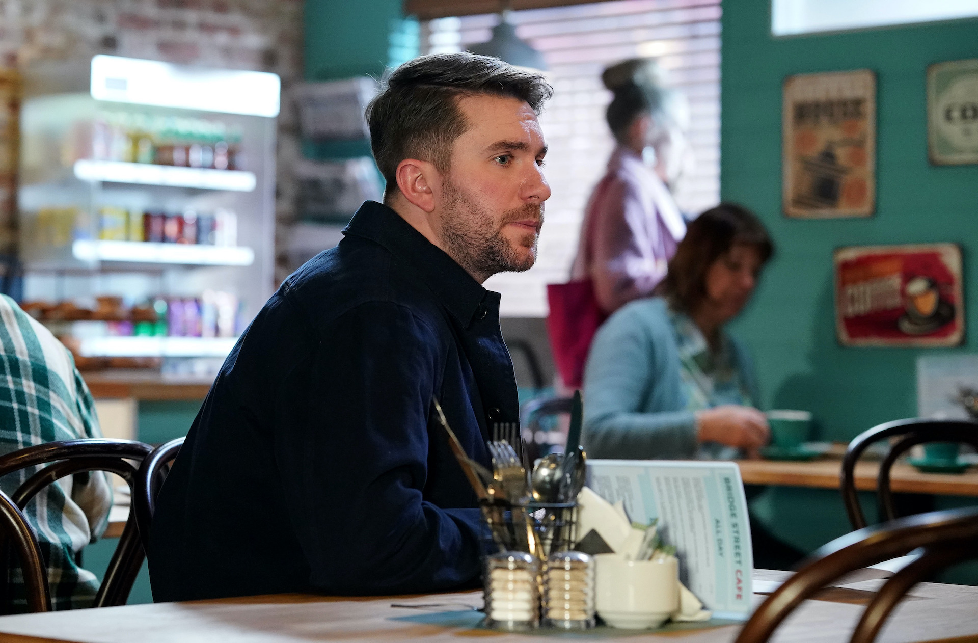 Callum sitting in the cafe with a sad look on his face 