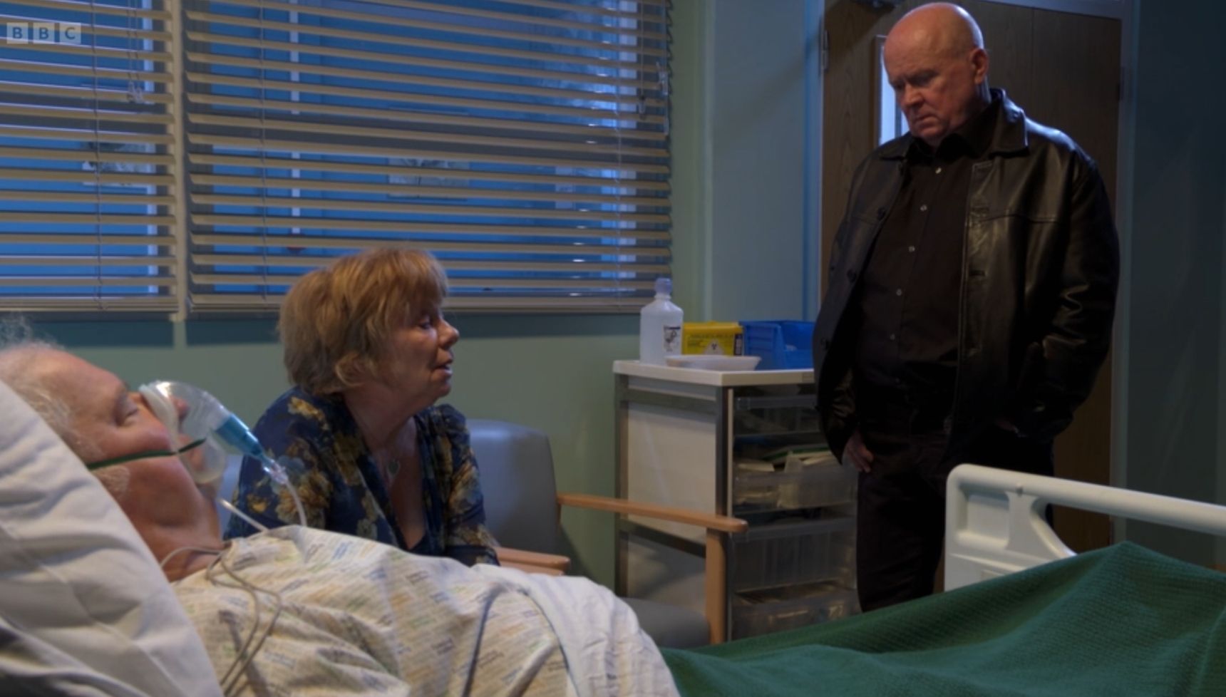 Phil and Julie sit around Nigel's hospital bed