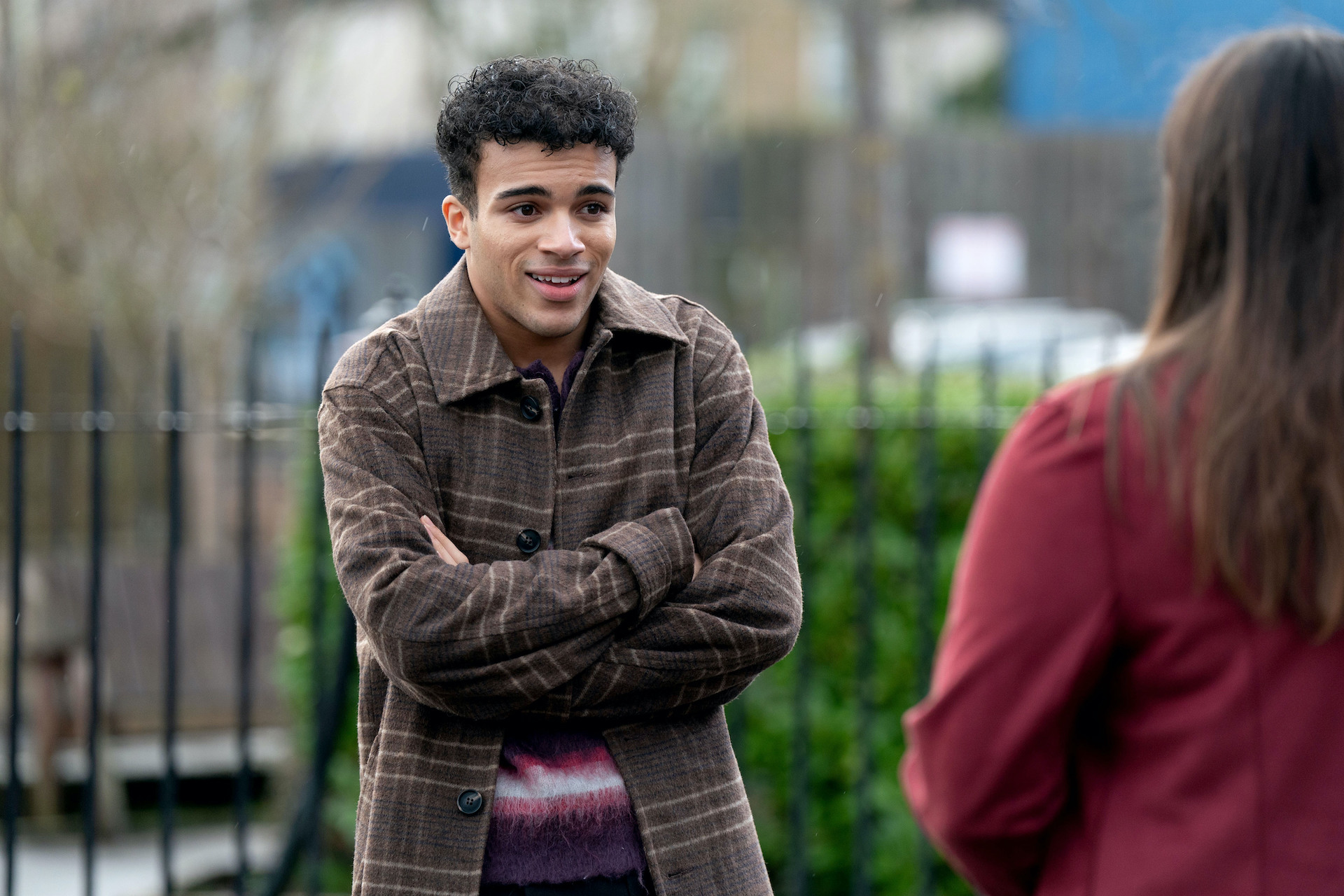 Josh standing with his arms crossed in the Square as he talks to Zoe 