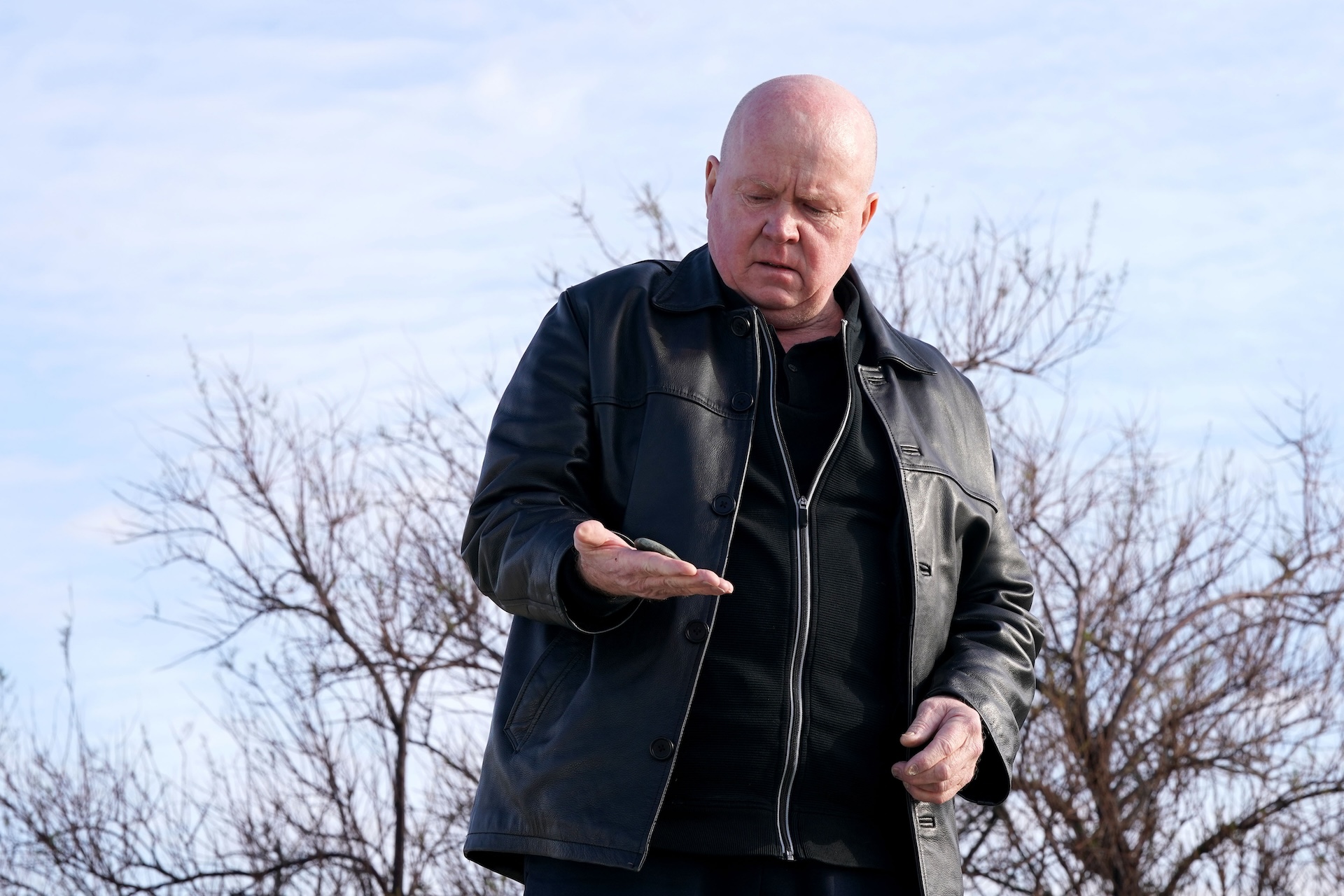Phil looking at a stone in his hand at the beach in EastEnders spoilers 