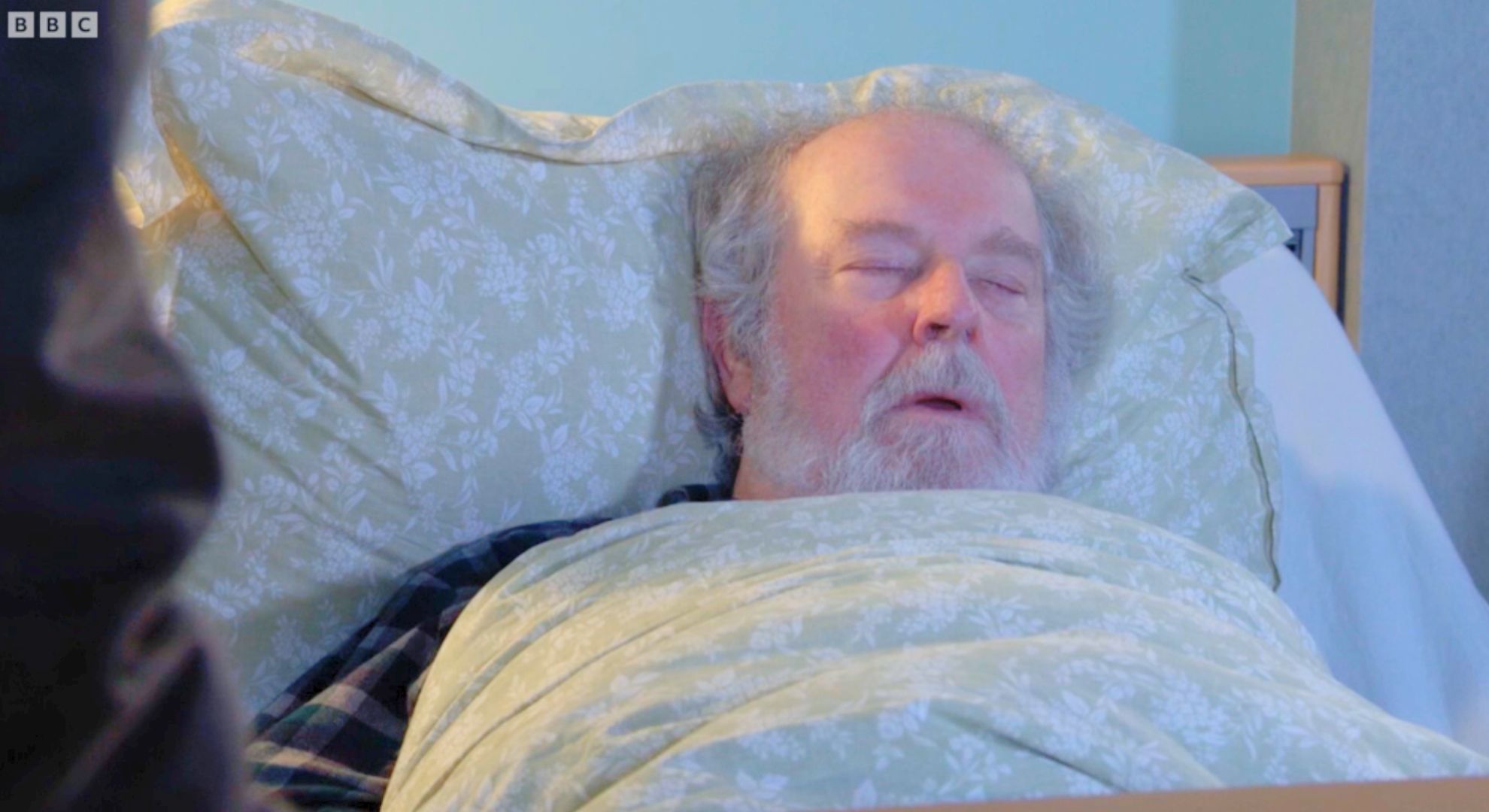 Lexi sitting by Nigel's bed as he sleeps in EastEnders