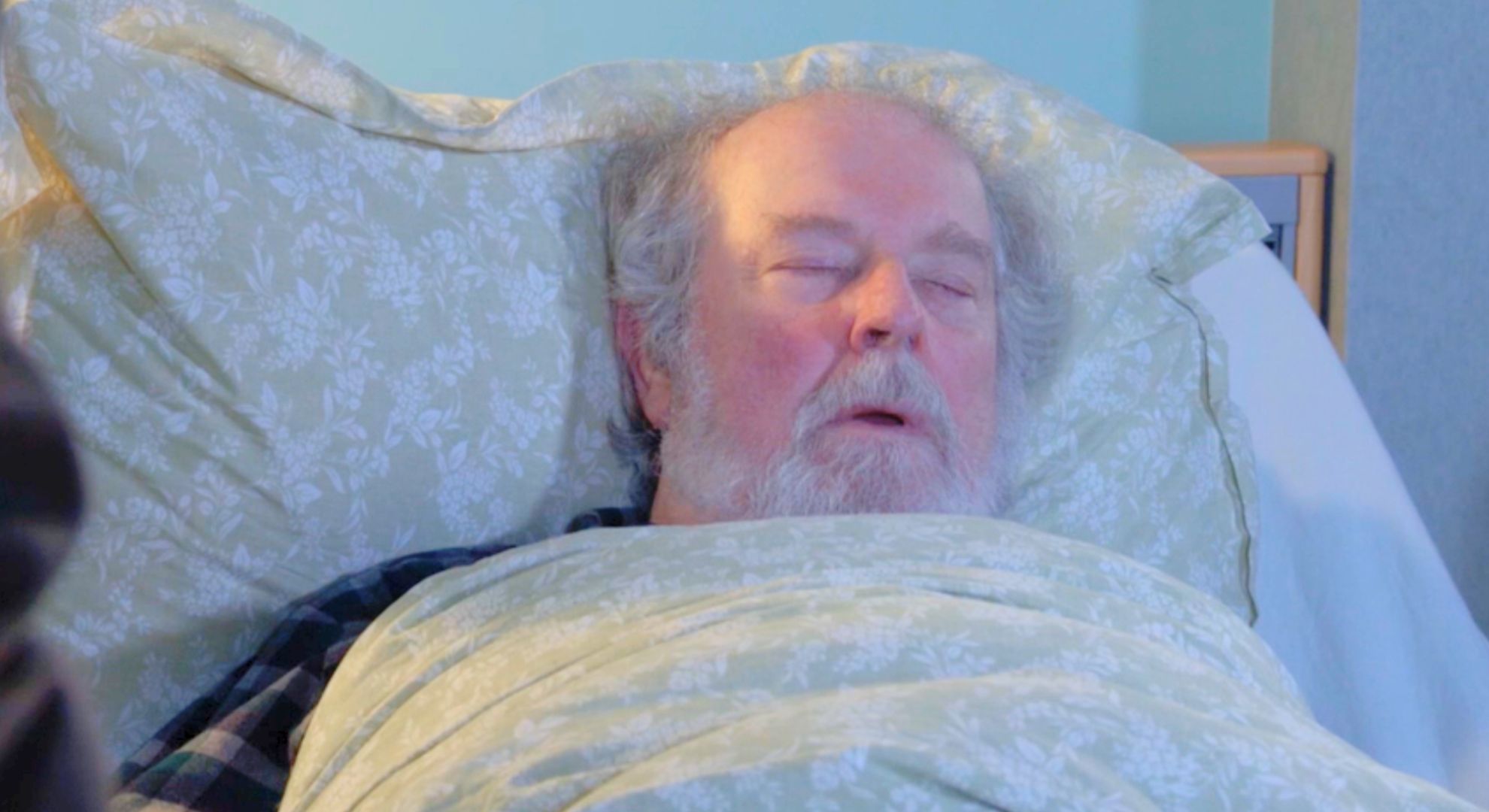 Julie sitting by Nigel's bed as he sleeps