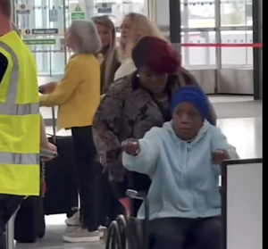 Denise is frail, in a wheelchair, and has her hair wrapped in a scarf 