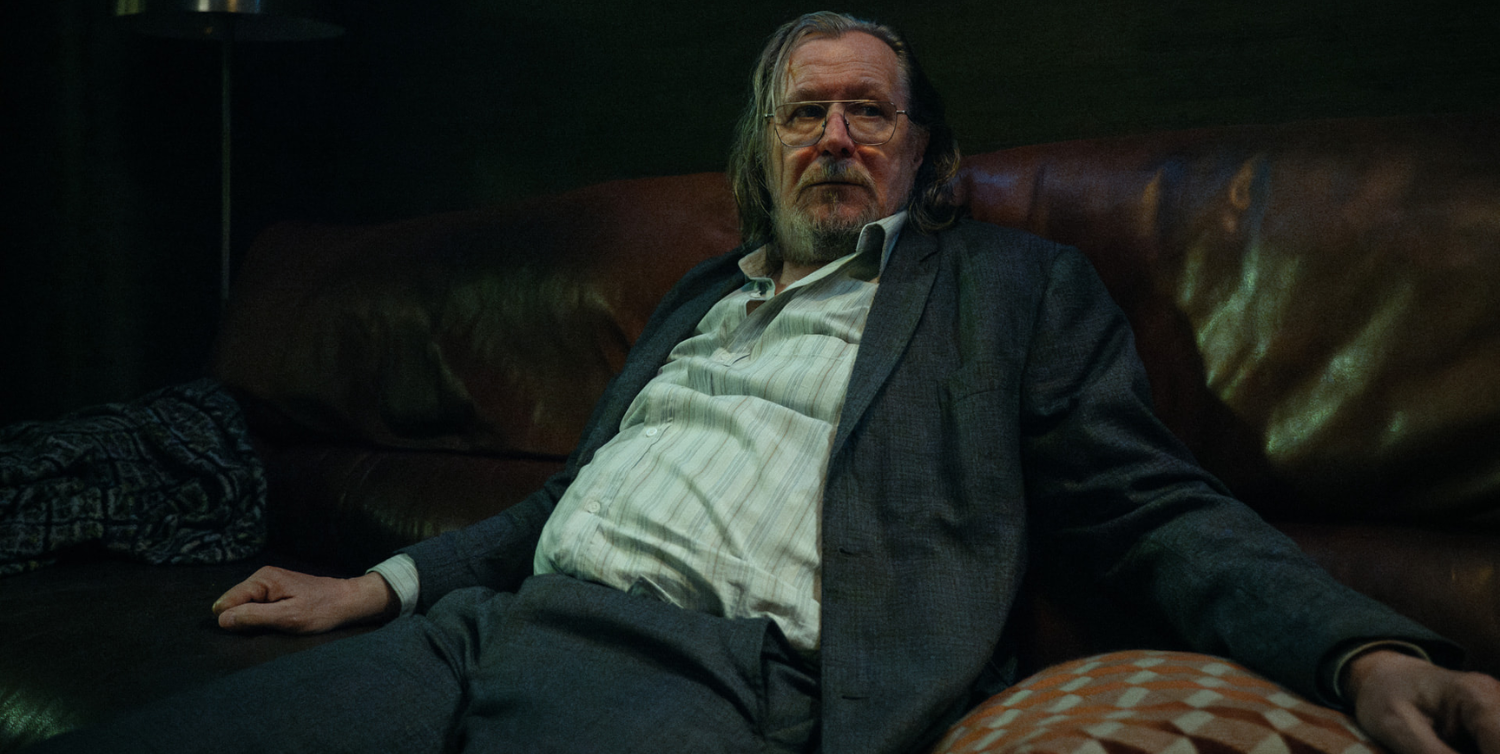 A close-up of Gary Oldman as Jackson Lamb in Slow Horses season 4, who is dressed in a suit and sat on a sofa.