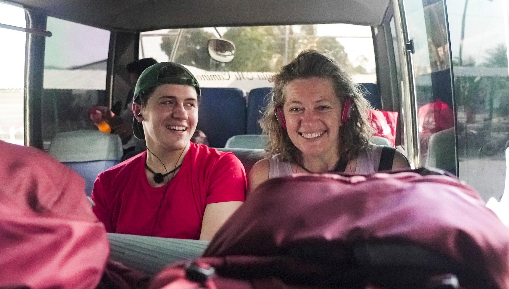 A young man in a red T-shirt and a woman with earphones in sit in a van