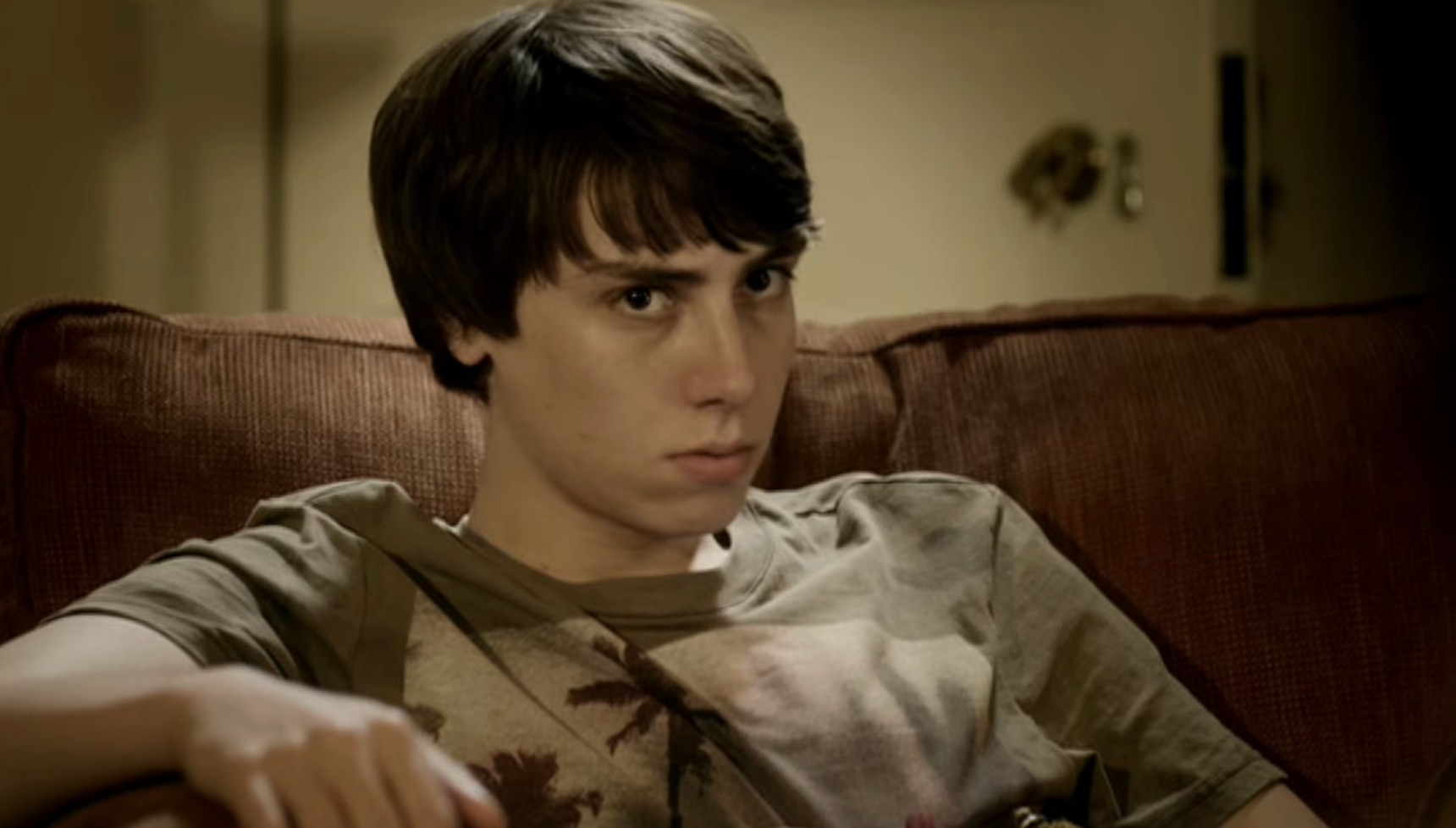 Long-haired teenager scowling whilst sat on the sofa