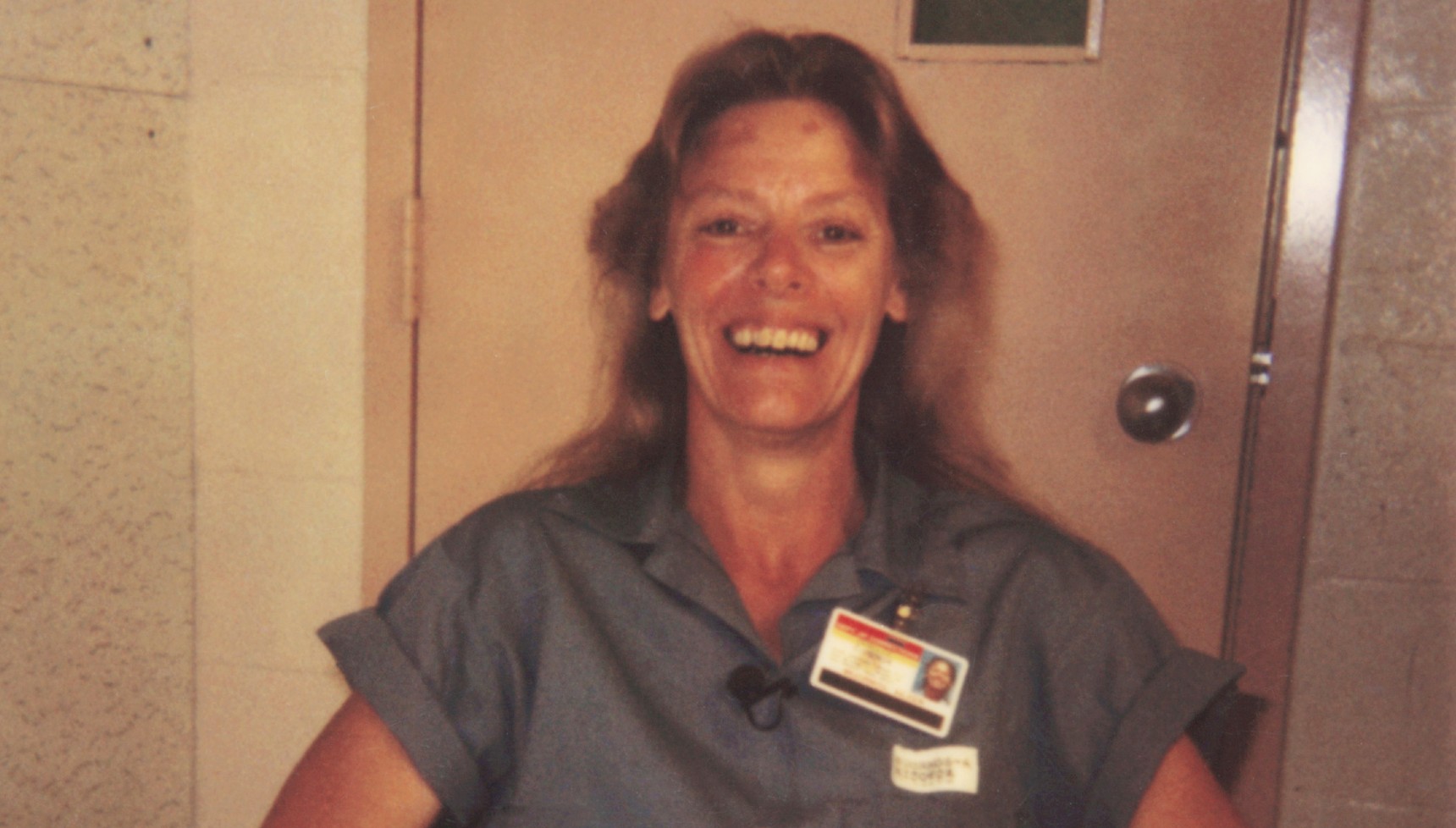 Blonde prison inmate smiles in a polaroid photo whilst sat on a chair