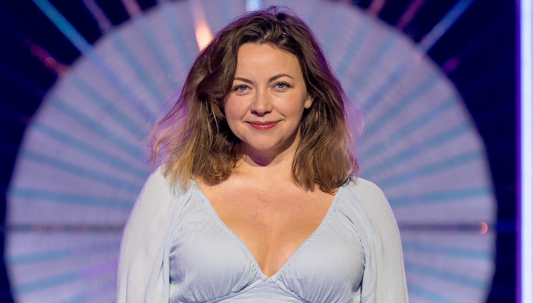 Woman in a light blue v-necked dress smiles into the camera
