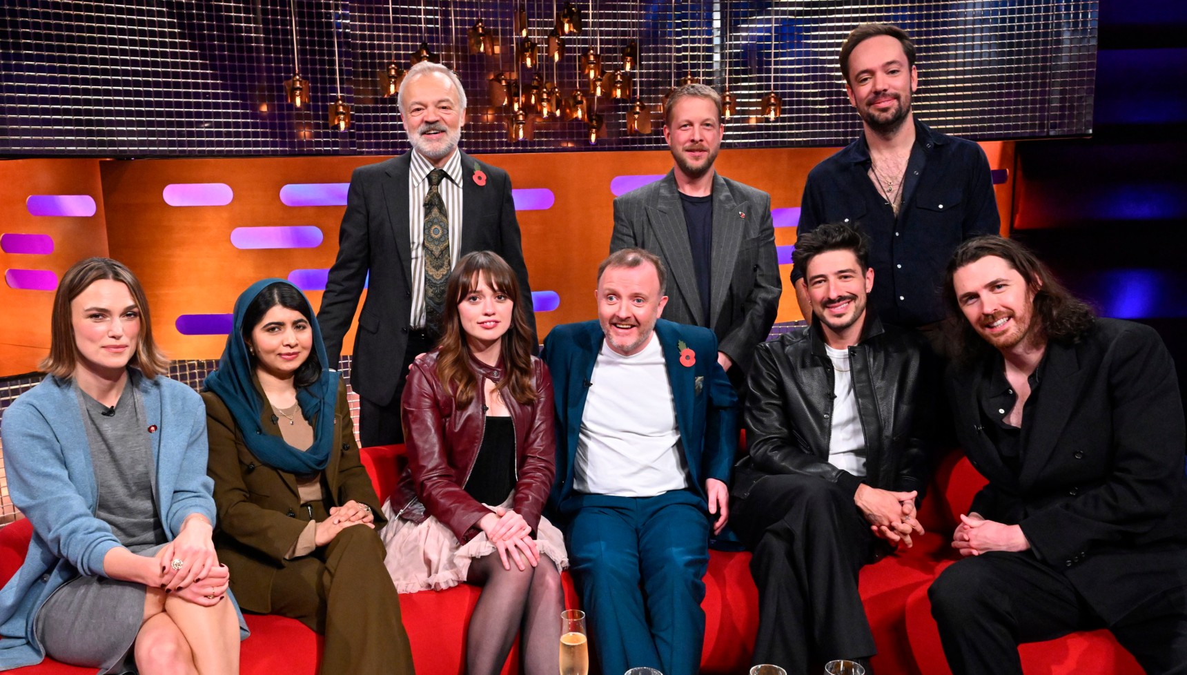 Keira Knightley, Malala Yousafzai, Graham Norton, Aimee Lou Wood, Chris McCausland, Mumford & Sons, and Hozier pose in the talkshow studio