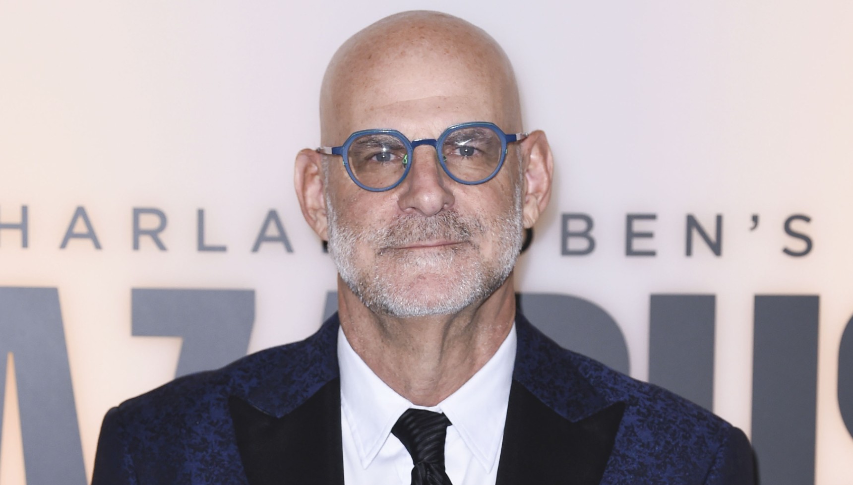 Harlan Coben wearing his distinctive blue-framed spectacles on the red carpet of a Lazarus screening