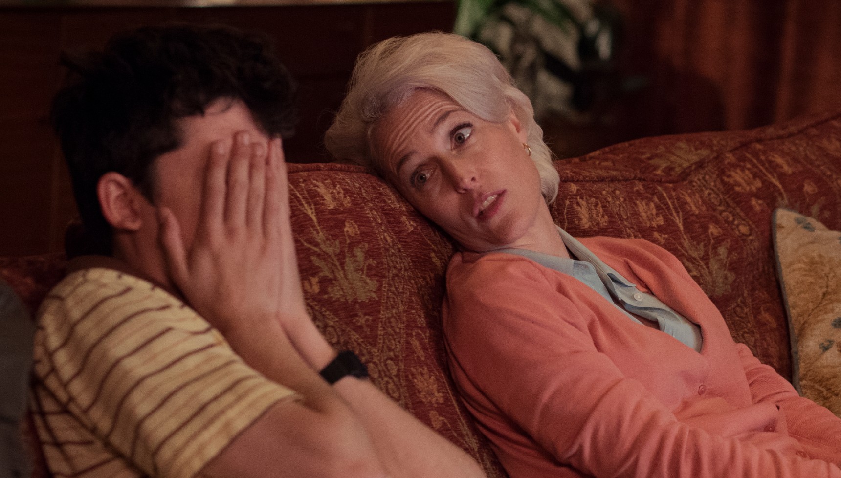 A teenager holds his face in his hands whilst speaking to his mum on the sofa