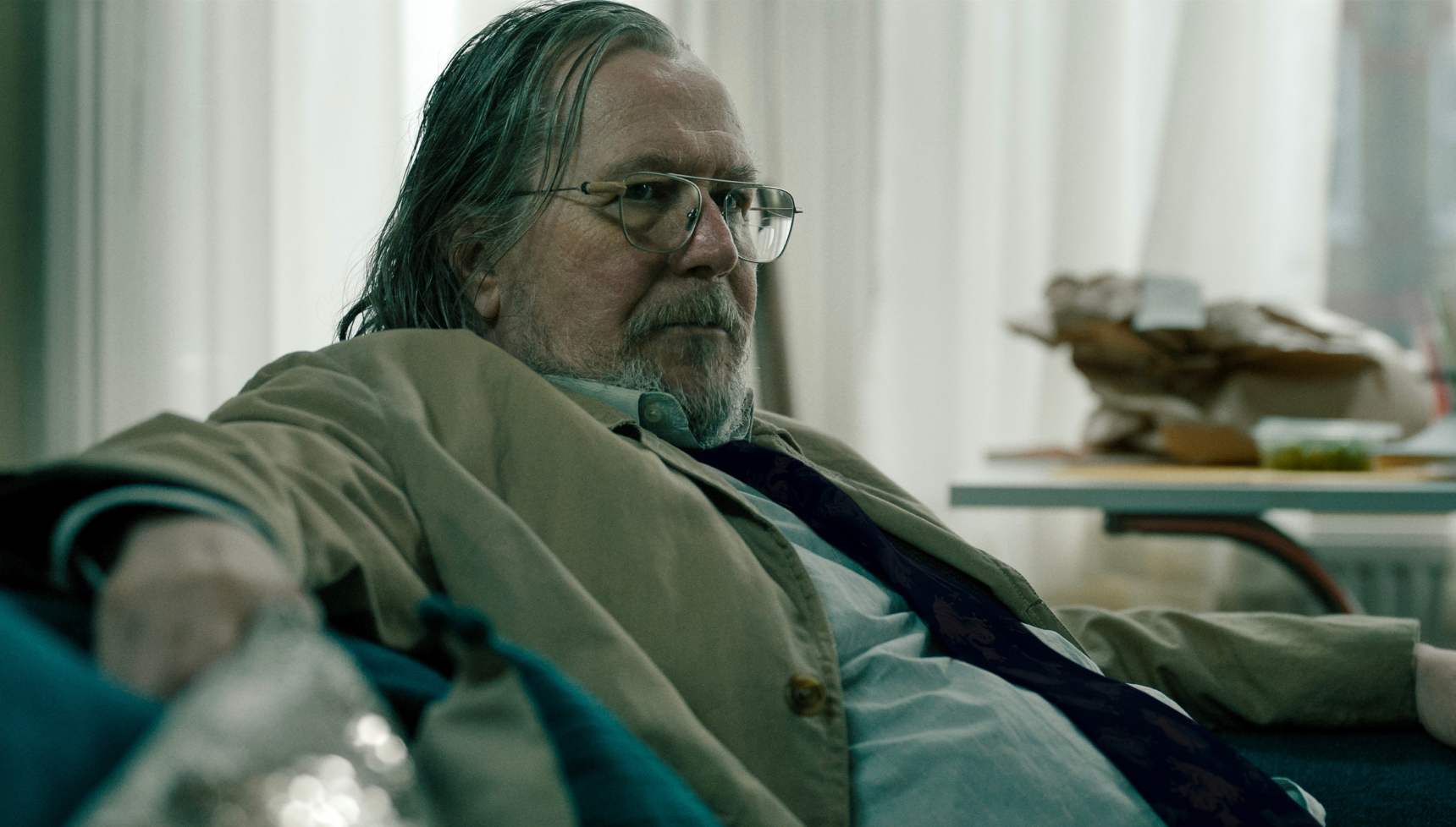 Close up of Gary Oldman sat on the sofa dressed as Jackson Lamb.