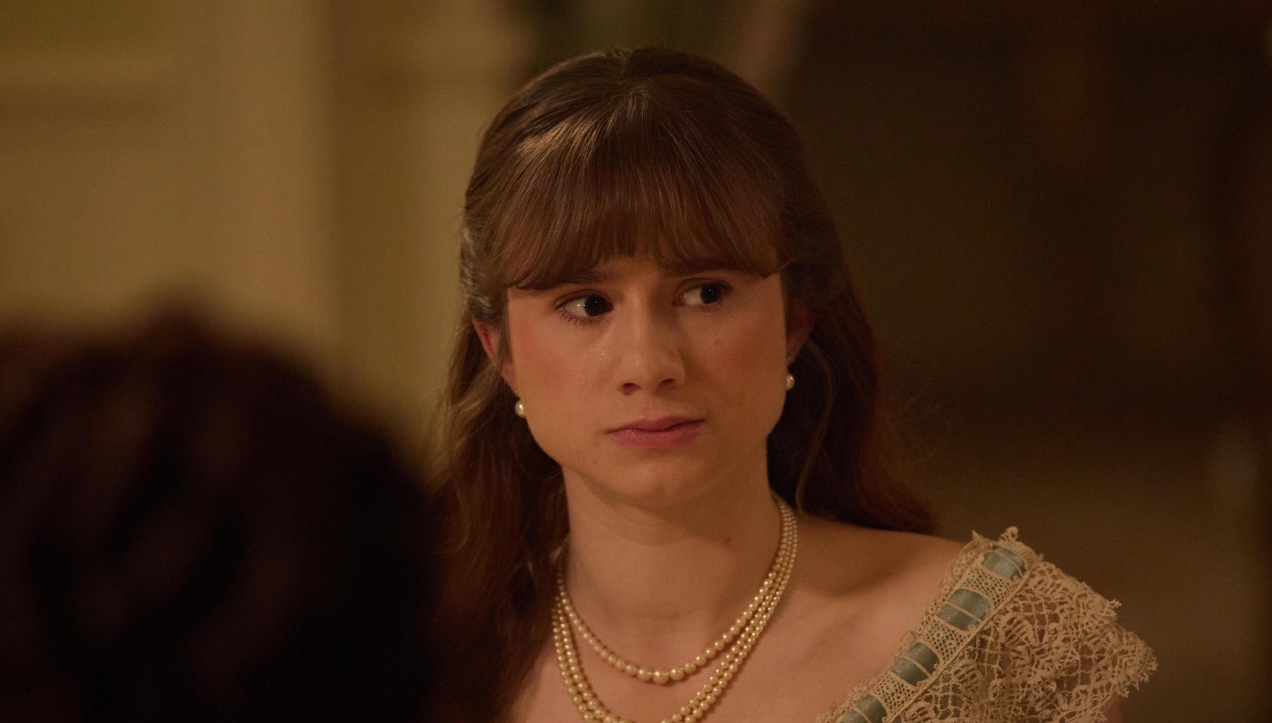Justine Moore as June looking to one side of her with while sitting at a dinner table