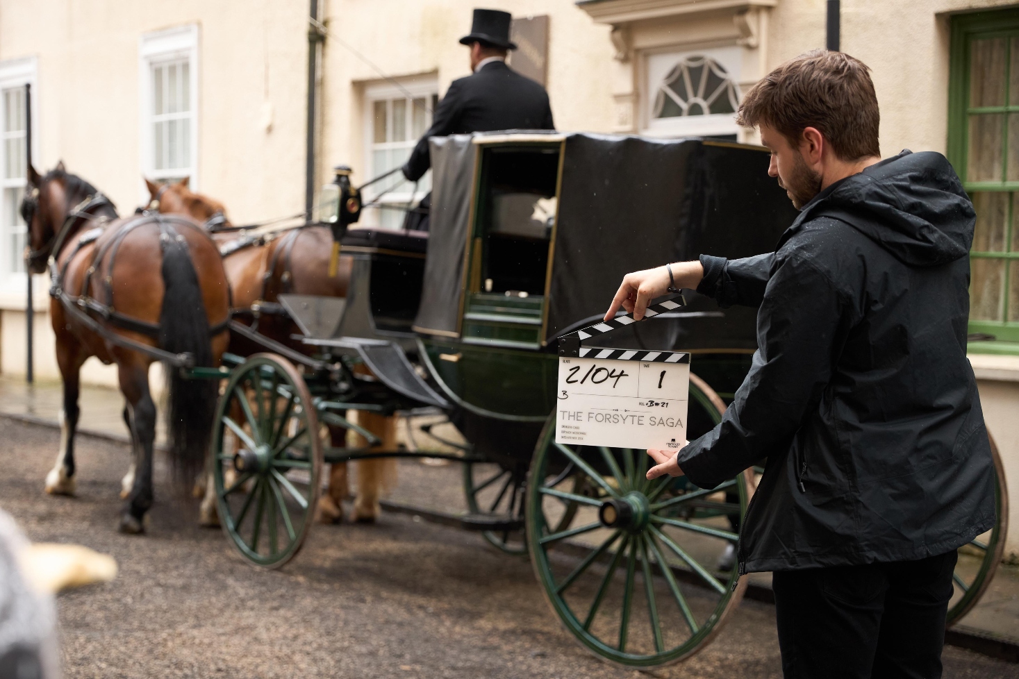 A man with a clapperboard standing in front of a Victorian horse and carriage.