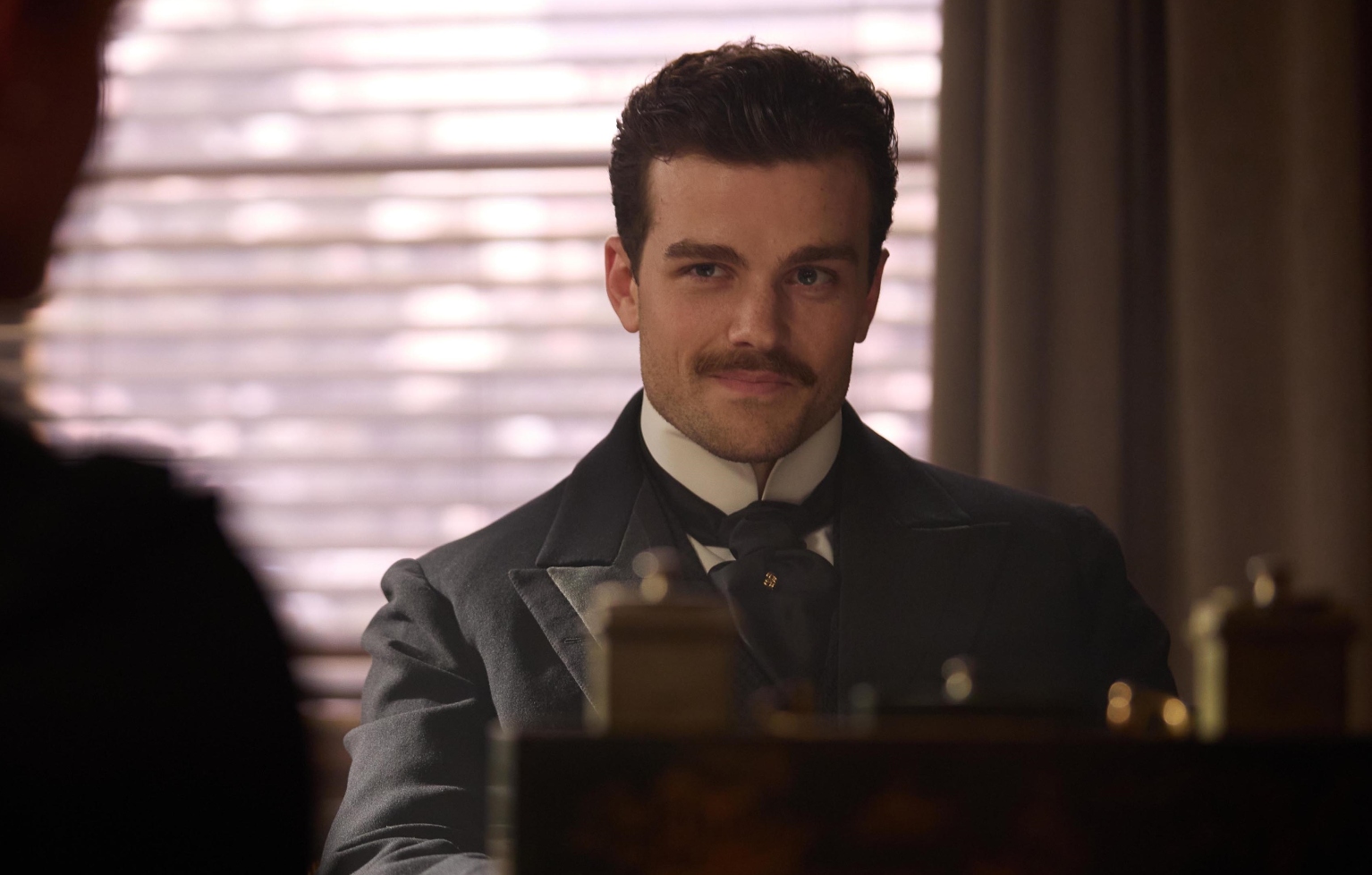 Joshua Orpin as Soames wearing a dark suit and sitting behind a desk in The Forsytes cast