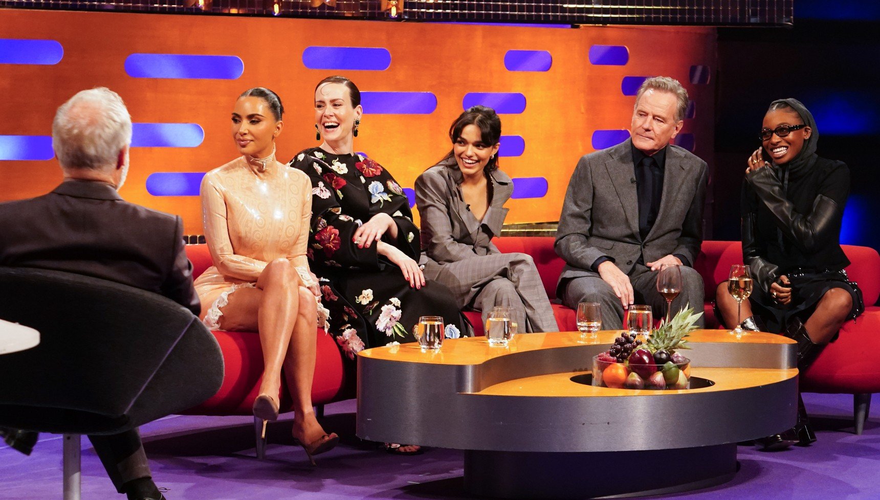 A talkshow host has his back to the audience as he talks to five celebrities on a couch