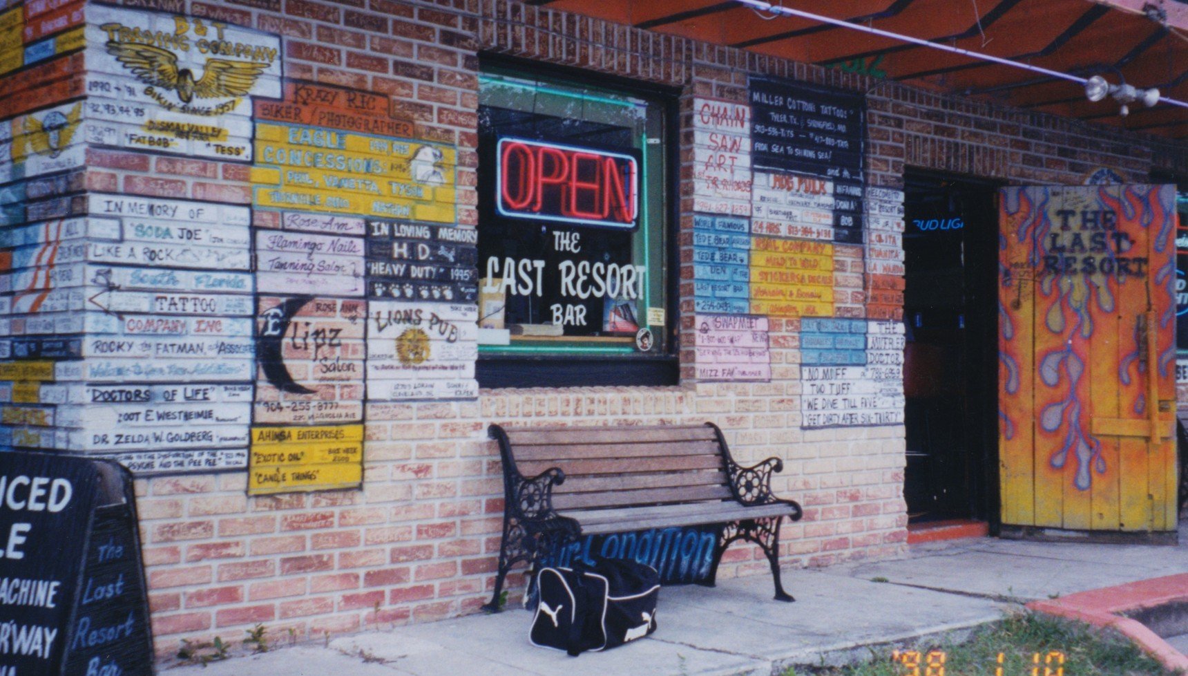 A graffiti-covered bar with its door swung open and a wooden bench outside it