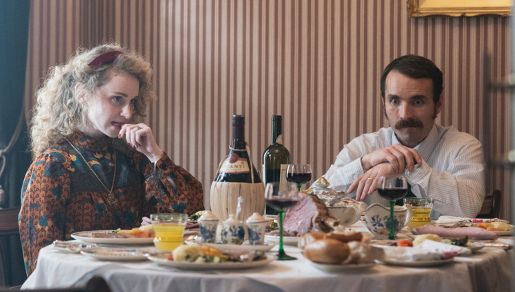 An awkward-looking couple sit at the dinner table