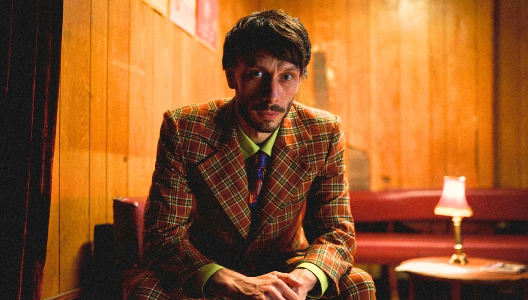 Richard Gadd wearing a suit and sitting in a comedy club in Baby Reindeer