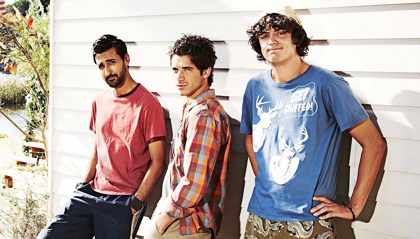 Arsher Ali, Sam Robertson, and John Dagleish leaning against a cabin wall in Beaver Falls