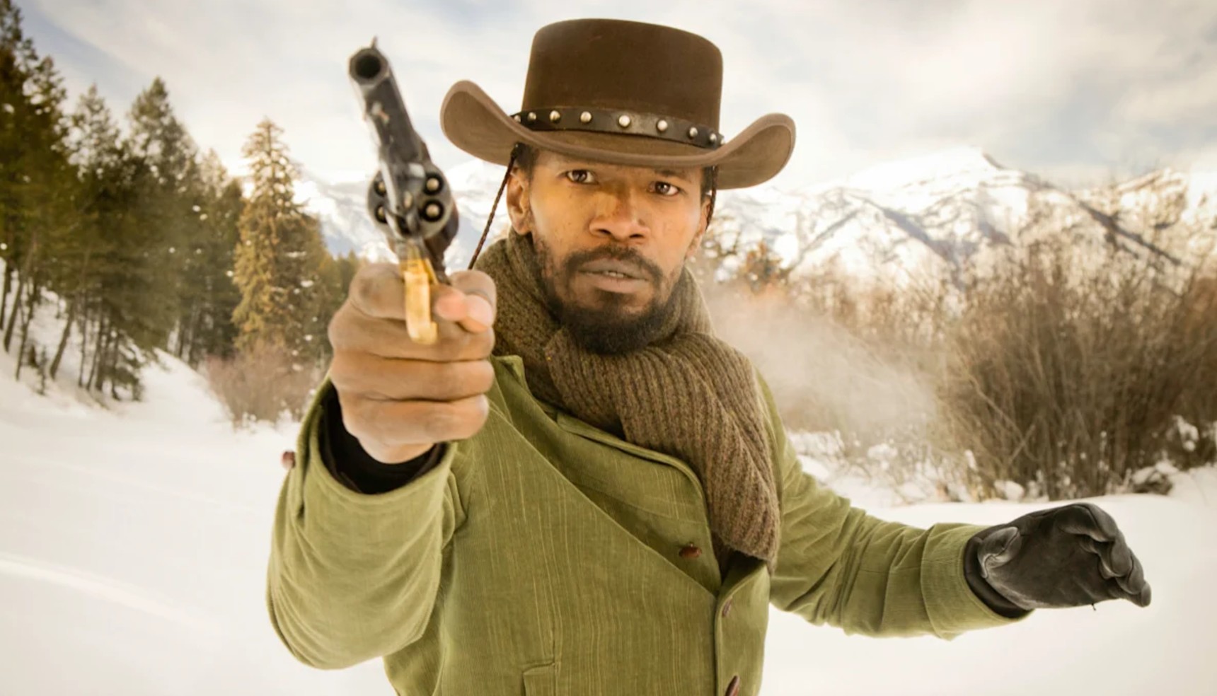 Jamie Foxx in a cowboy hat and pointing a gun while standing in the snow in Django Unchained