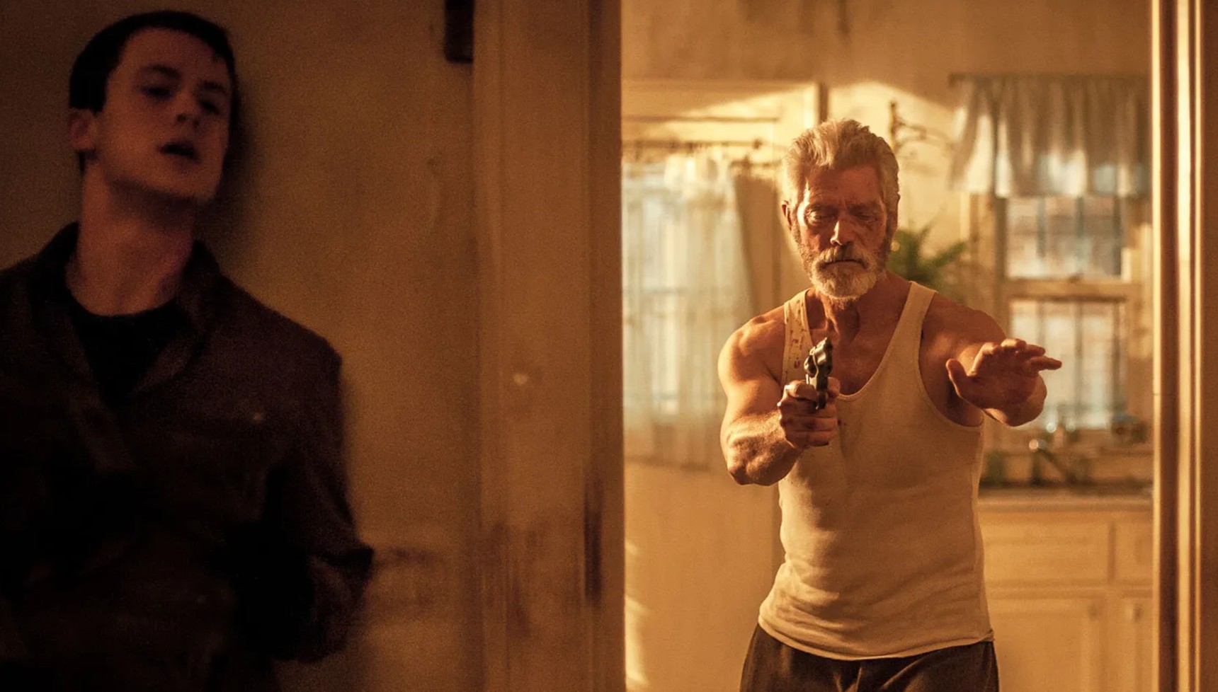Dylan Minnette hiding around a corner from Stephen Lang as he holds a gun in Don't Breathe