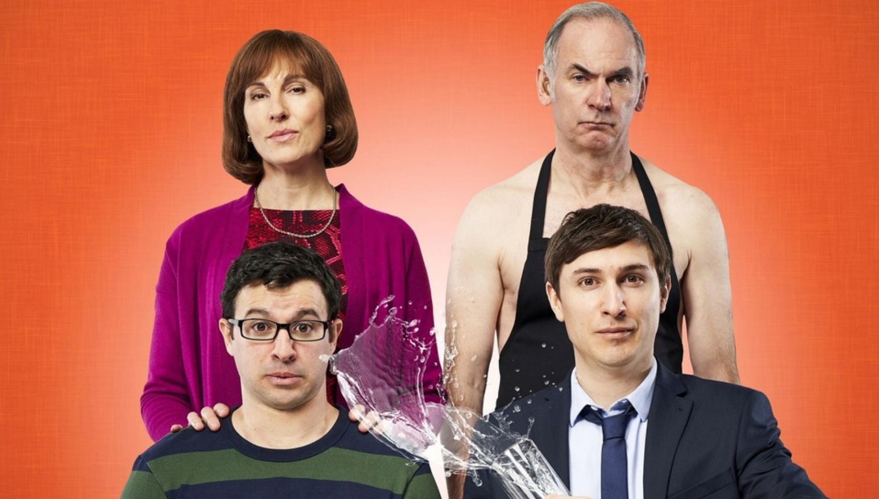 Tamsin Greig and Paul Ritter standing above Simon Bird and Tom Rosenthal as he throws a glass of water