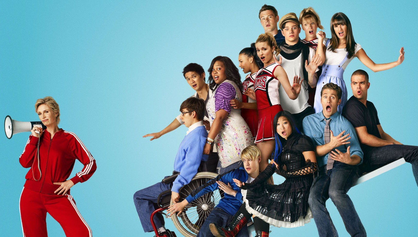Jane Lynch with a megaphone next to the cast of Glee on a bench