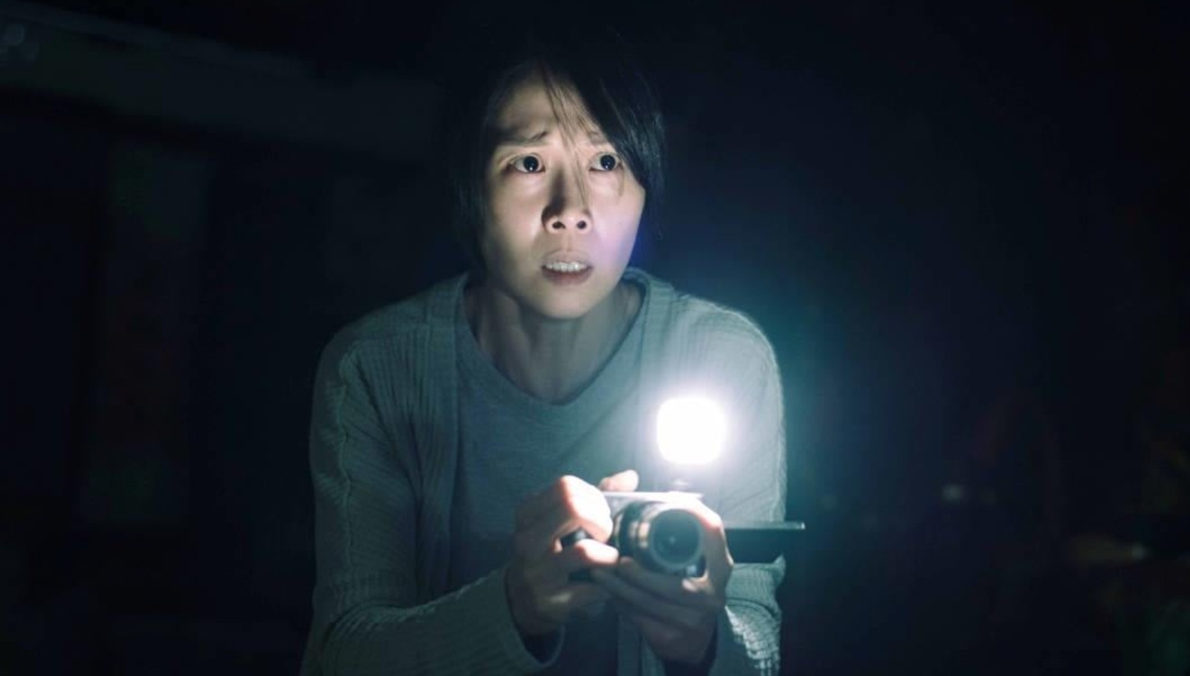 A woman holding a camera with a flashlight in Incantation