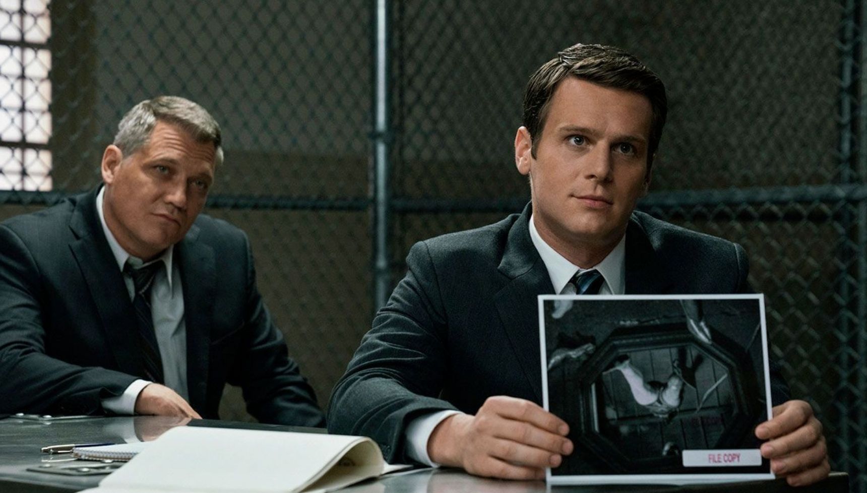 Holt McCallany sitting behind Jonathan Groff as he holds an x-ray in Mindhunter