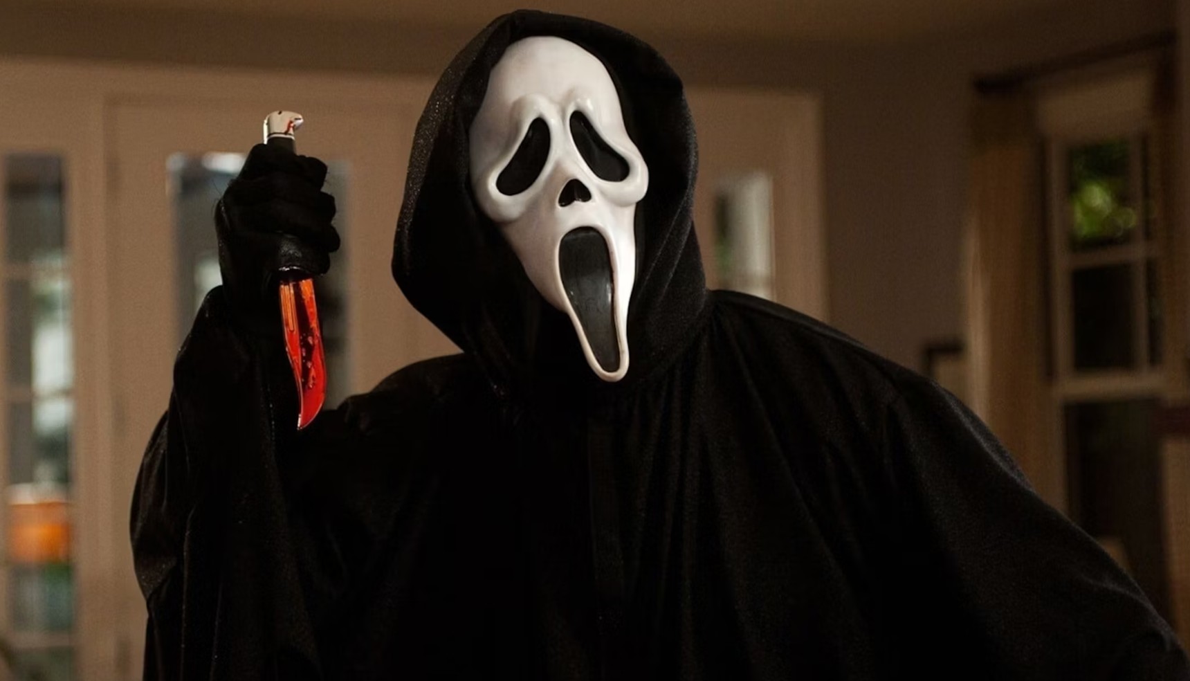A masked man in a black cloak holding a bloody knife in Scream