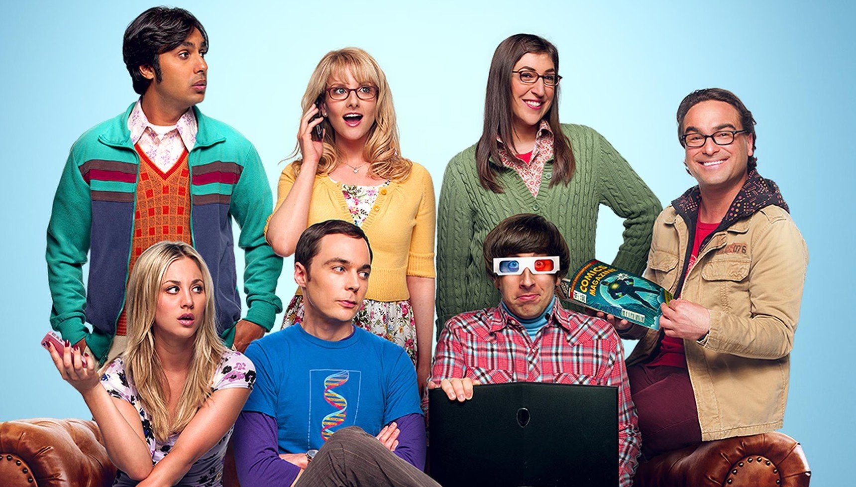 Raj, Bernadette, and Amy standing above Penny, Sheldon, Howard, and Leonard as they sit on the sofa in a promotional image from The Big Bang Theory