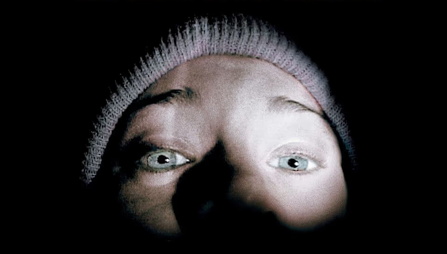 Heather looking at the camera with a flashlight on her face on the poster for The Blair Witch Project