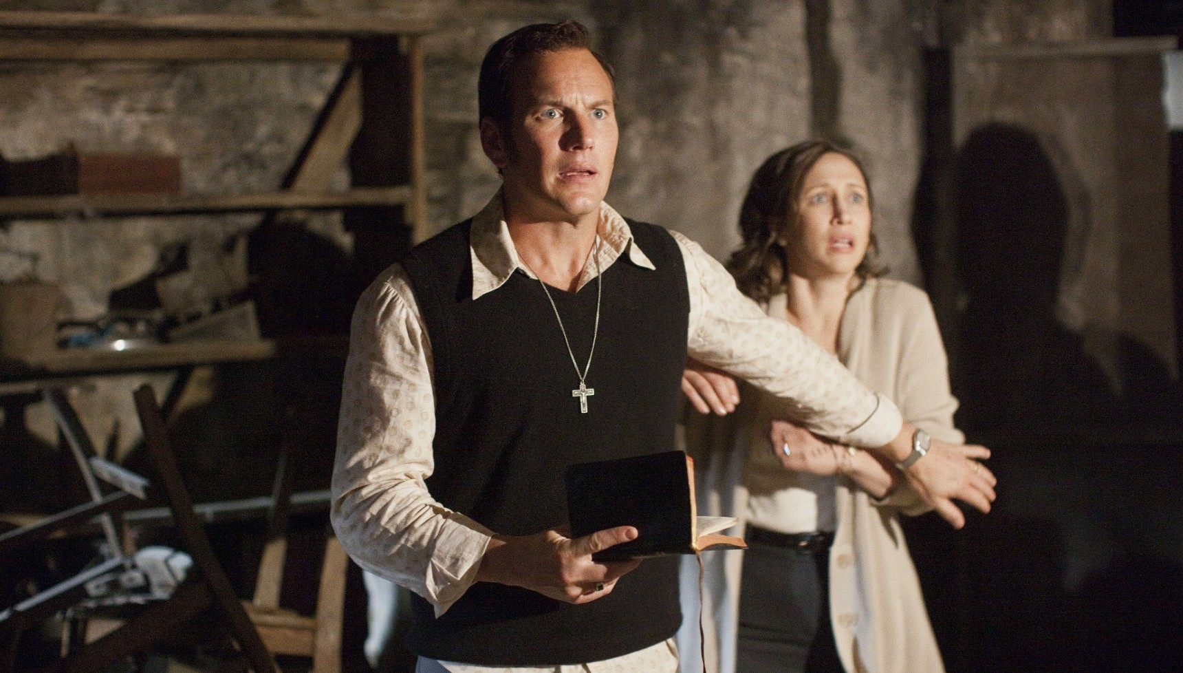Patrick Wilson as Ed Warren holding back Vera Farmiga's Lorraine Warren as he holds a Bible in The Conjuring