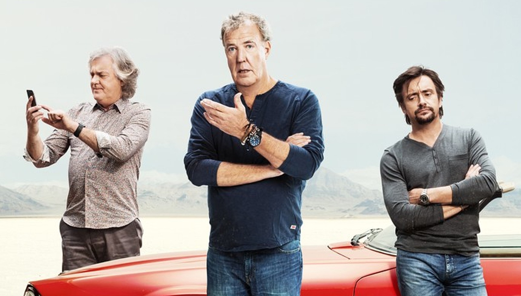James May looking at his phone as Jeremy Clarkson and Richard Hammond look at the camera in front of a car in The Grand Tour