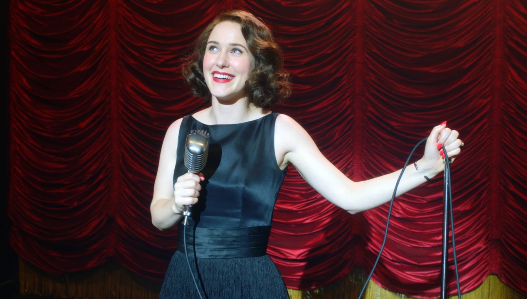 Rachel Brosnahan holding a microphone on stage in The Marvelous Mrs Maisel