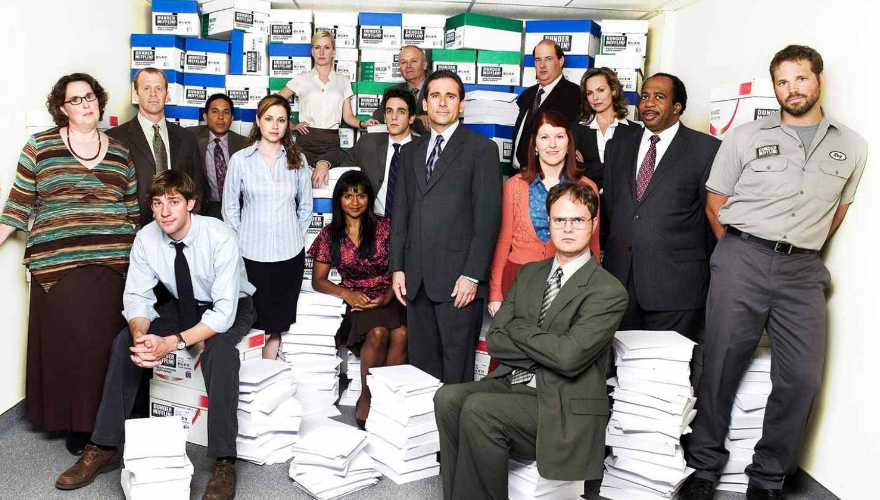 The cast of The Office (US) standing in front of stacks of paper