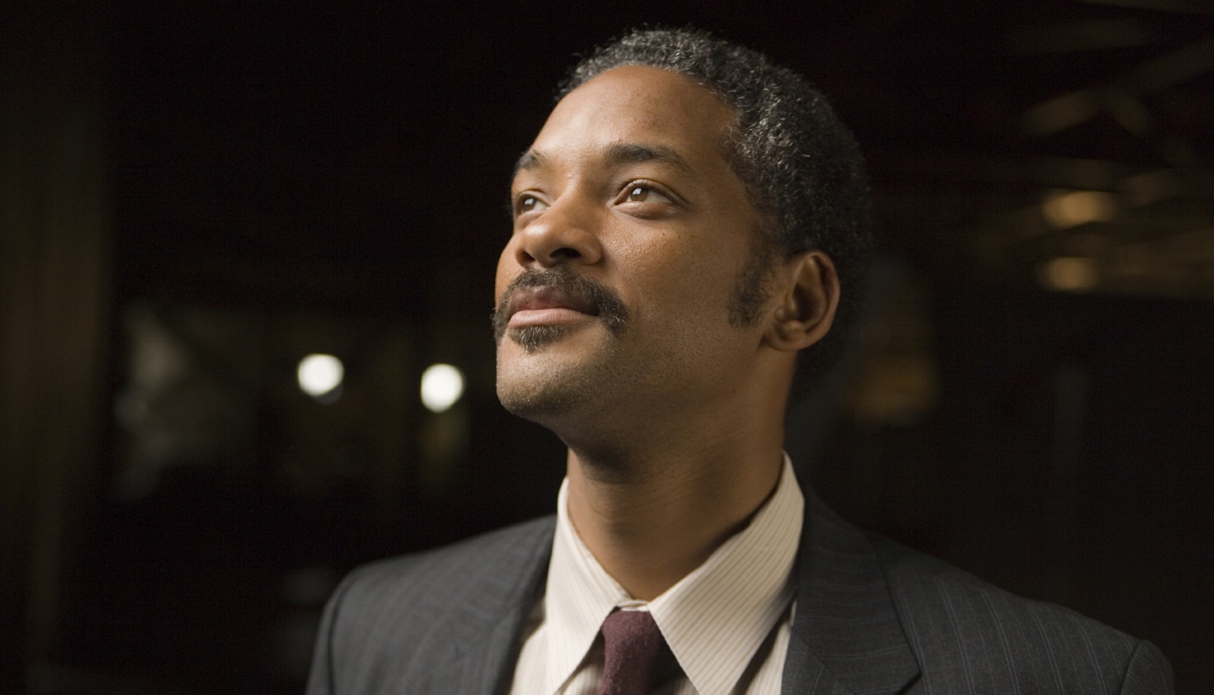Will Smith in a suit smiling as looks into the distance in The Pursuit of Happyness